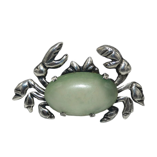 Silver crab-shaped brooch with a green stone on a white background