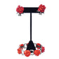 Red floral earrings on a black stand against a white background