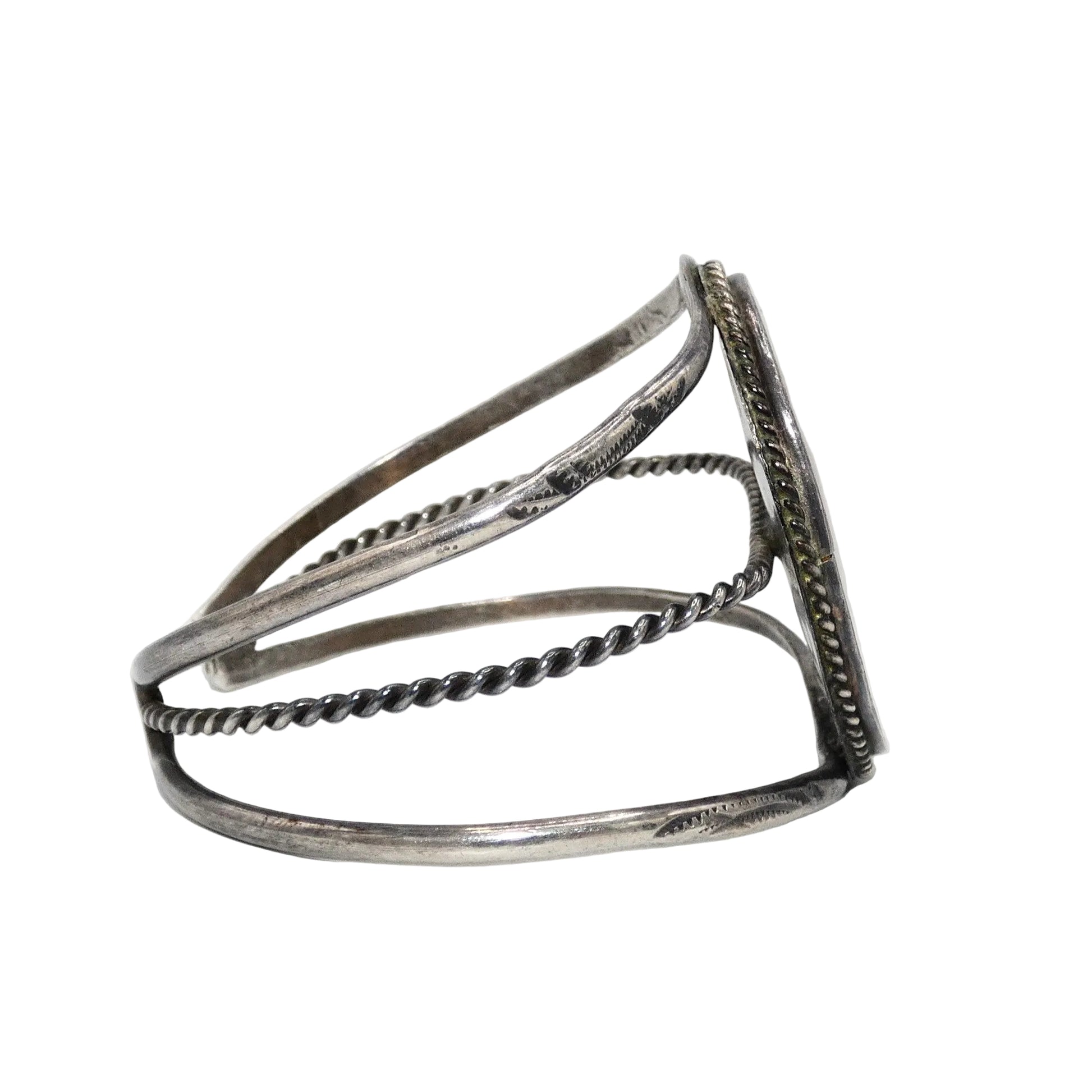 A silver-toned open cuff bracelet with textured twisted wire bands and a flat rectangular end featuring engraved detailing