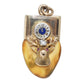 An elk tooth with 10k gold featuring an elk head motif with a circular clock face at the top, accented with a blue enamel center, a clear central stone, and two pink gemstones in the eyes
