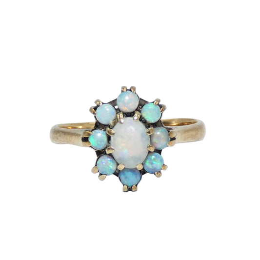 A 10k gold ring featuring a central oval white opal surrounded by eight smaller round iridescent opal stones, held by gold prongs on a gold band.