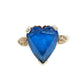 A heart-shaped blue topaz ring set in a 10K gold band with decorative filigree side details in the shape of a heart on both sides