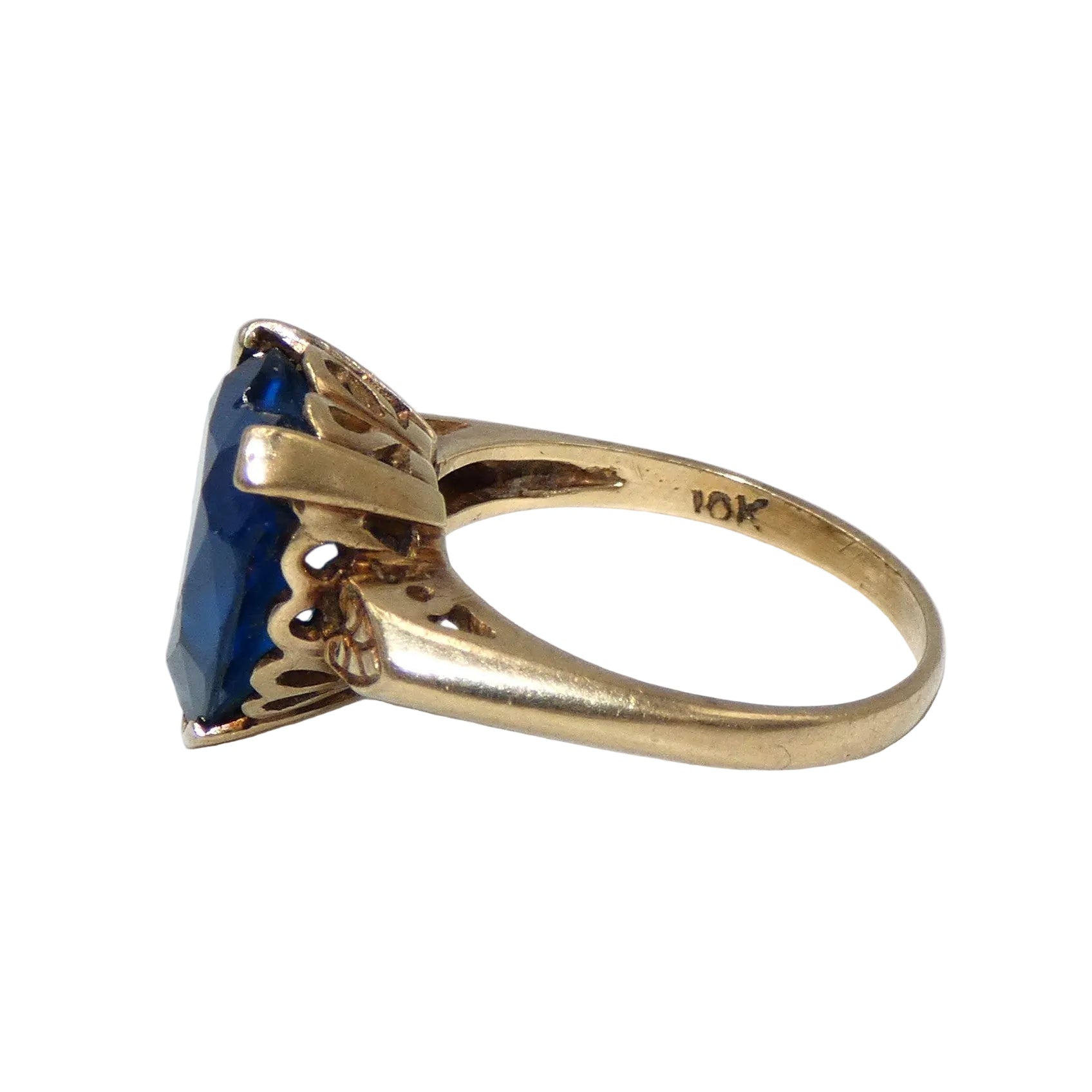 A heart-shaped blue topaz ring set in a 10K gold band with decorative filigree side details in the shape of a heart on both sides