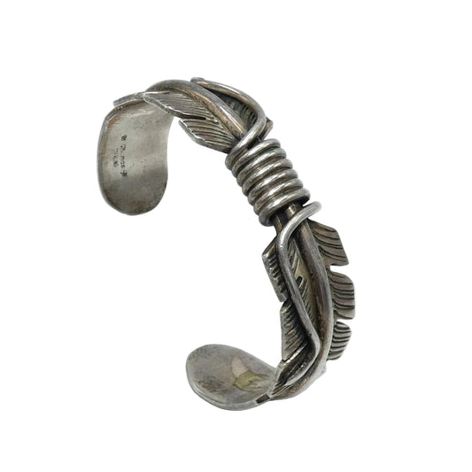 A sterling silver cuff bracelet with a detailed feather design and a wrapped spiral section