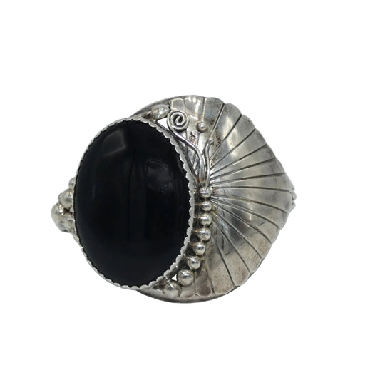 A silver cuff bracelet featuring a large, smooth onyx stone, set in an Art Deco style with scalloped and ribbed details