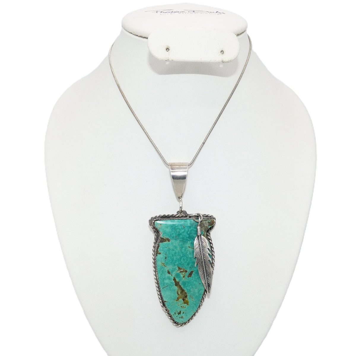 A silver necklace with a turquoise arrowhead pendant and a feather detail